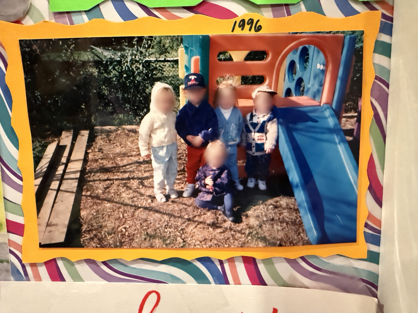 Family album photograph marked 1996: children gathered beside a playground slide, with their faces obscured.